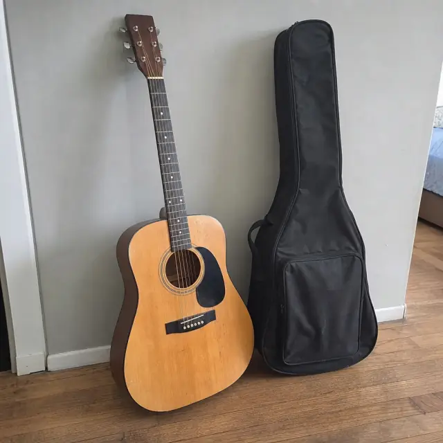Acoustic guitar next to its black soft case