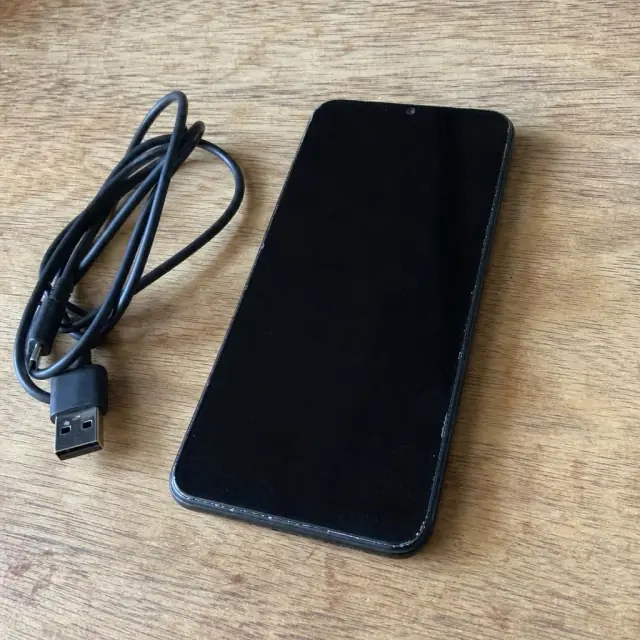 Black smartphone and a charging cable on a wooden table